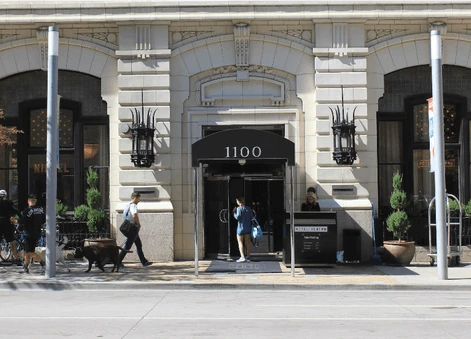 A street-level view of the ornate stone facade and entrance to a building with the address "1100" on a black awning.